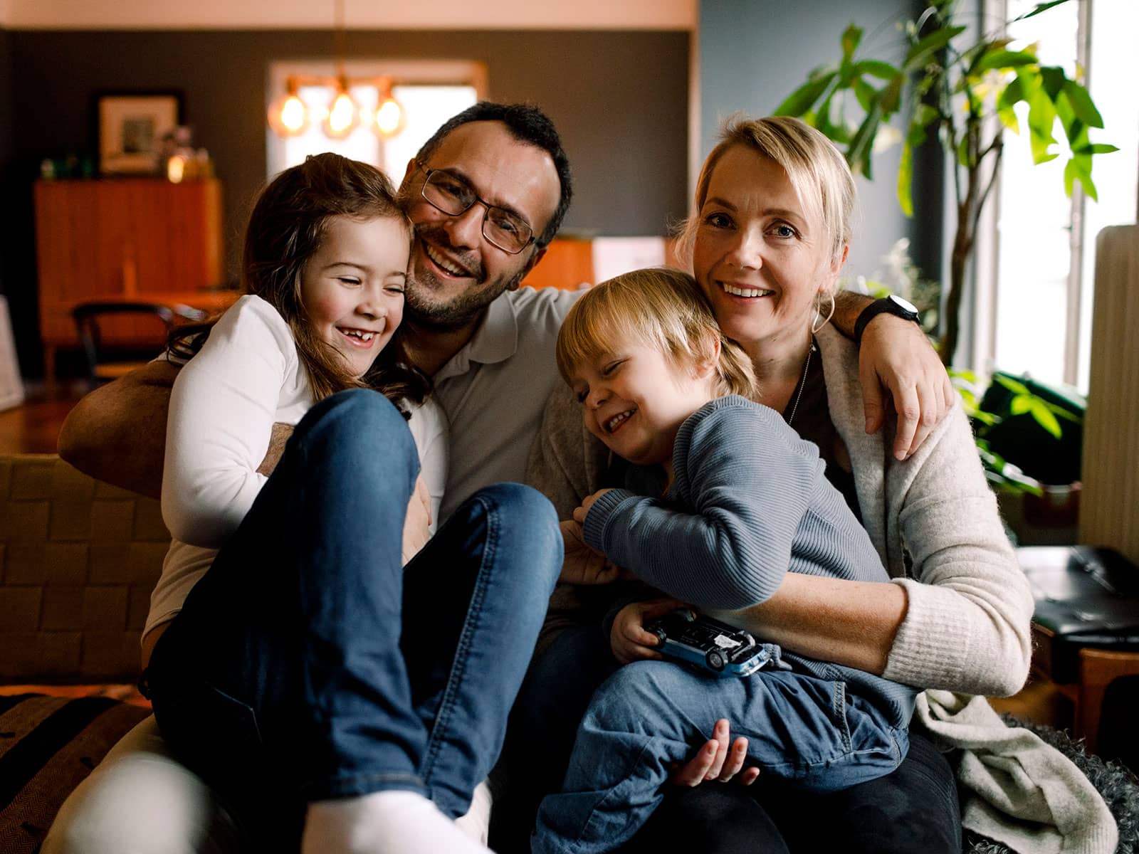 Familie sidder sammen i sofa. Hvor stort strømforbrug har din husstand? Se det typiske elforbrug for en gennemsnitsfamilie.