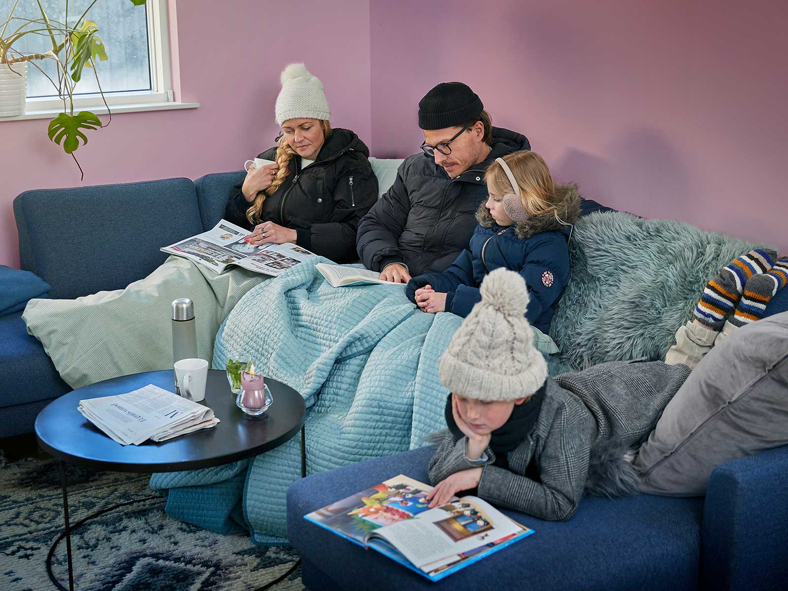 Familie sidder i sofa med overtøj og tæpper på. De fryser.