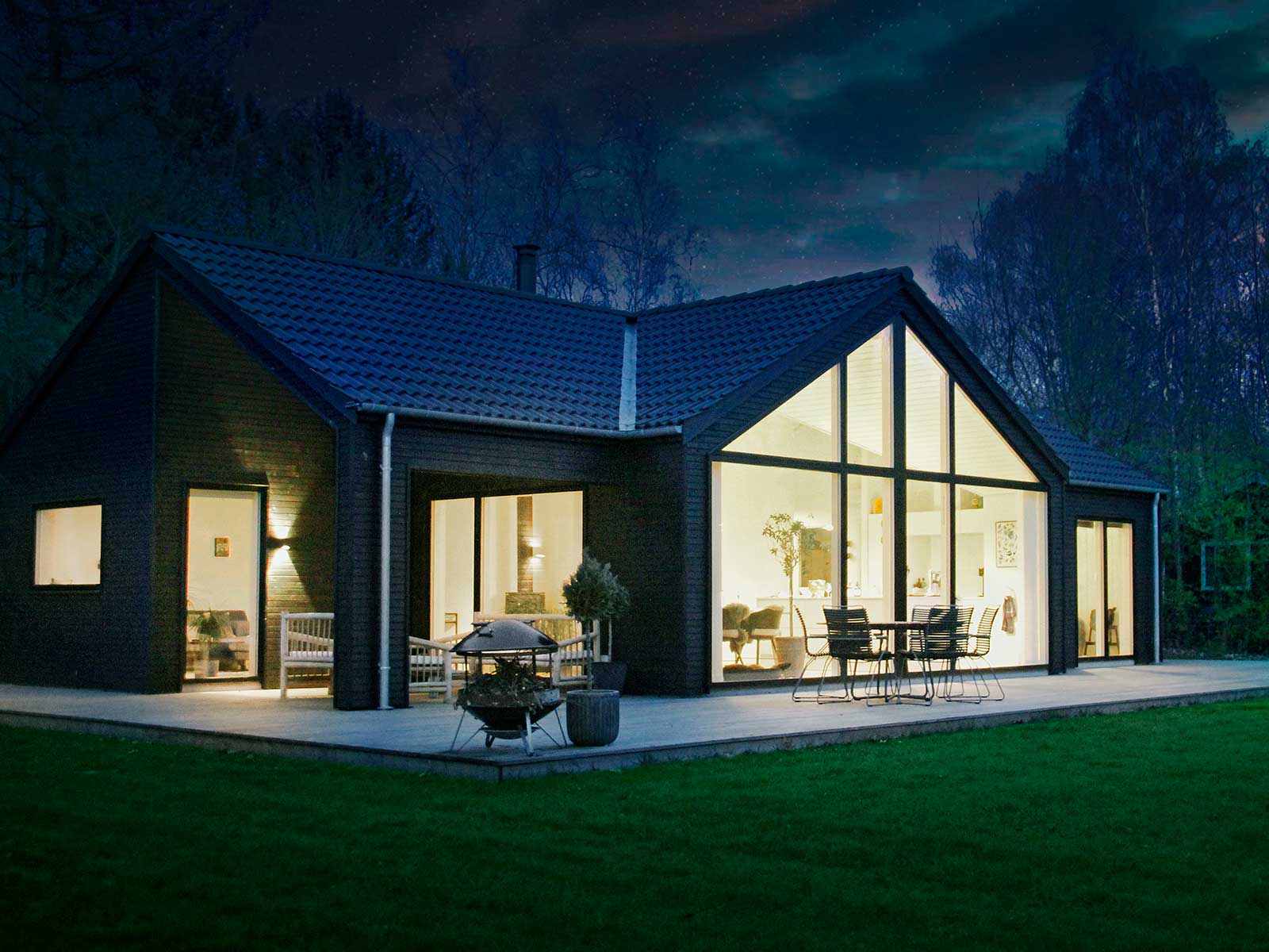 Moderne sommerhus med lys i vinduerne om aftenen.