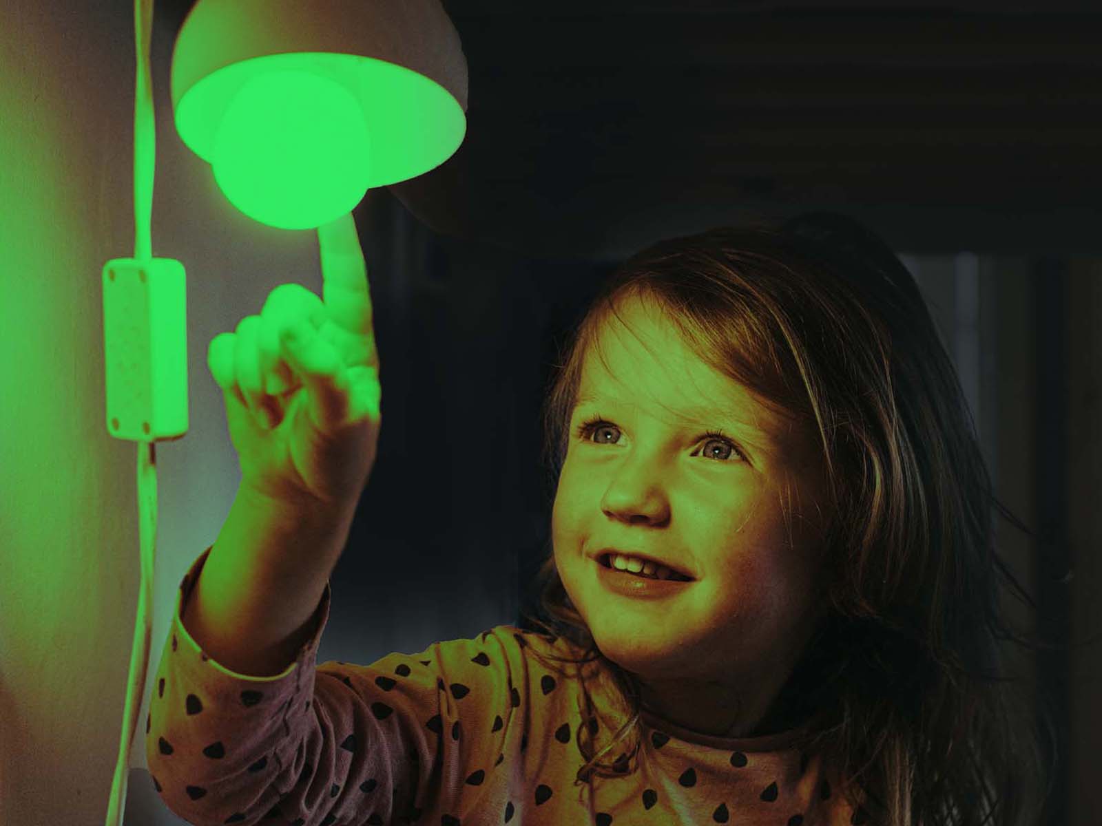 Pige står i grønt skær under lampe. Følg udviklingen i elpriser time for time, så du kan planlægge dit elforbrug, så du bruger strøm, når den udleder mindre CO2. 