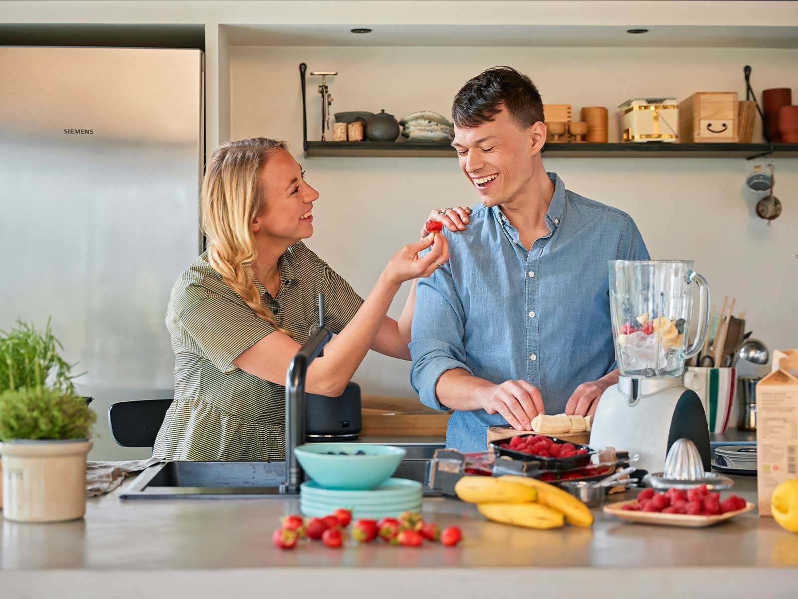 Ungt par står i køkken med madvarer og blender.