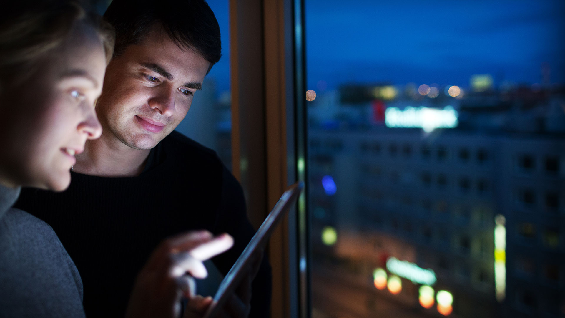 En ung mand og en kvinde står ved vinduet en aften og kigger sammen på en iPad. De har en elaftale med flexafregning.