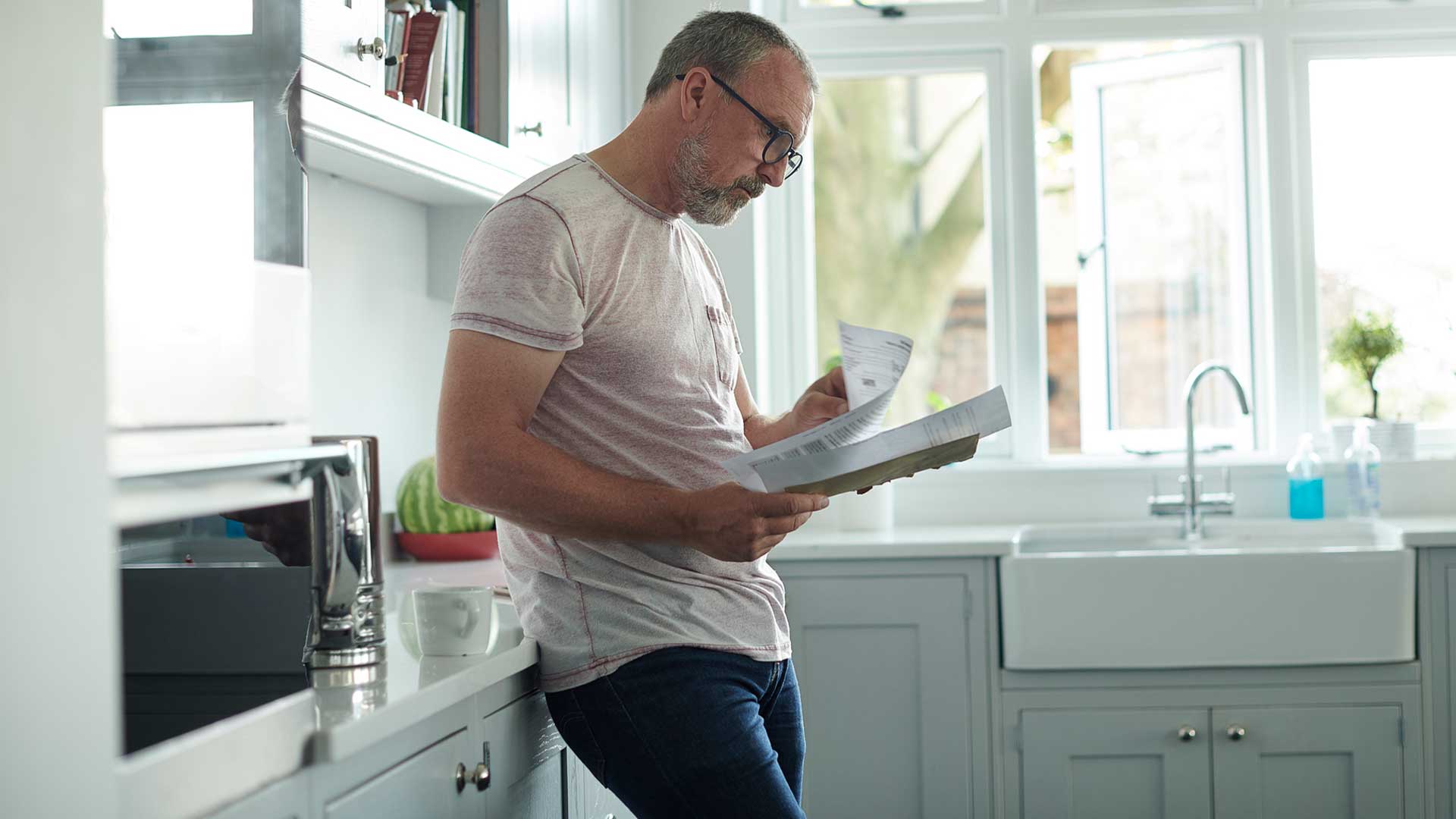 Mand kigger på sin elregning i sit køkken, og glæder sig over månedlig betaling hos sit elselskab. Der er ingen aconto hos EWII.