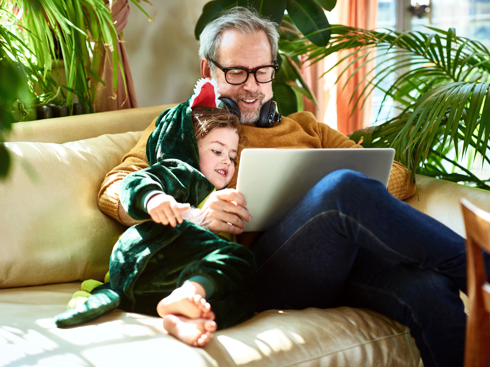 Bedstefar sidder med barnebarn iklædt dinosaurkostume og kigger på pc