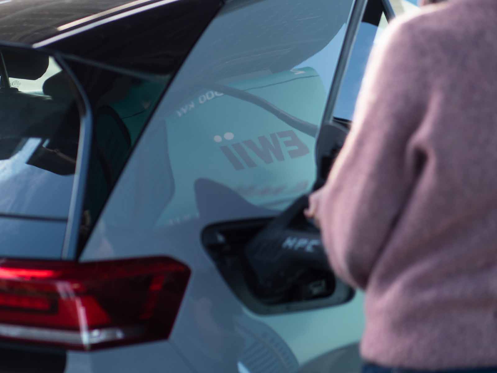Person oplader elbil med refleksion af EWII-logo
