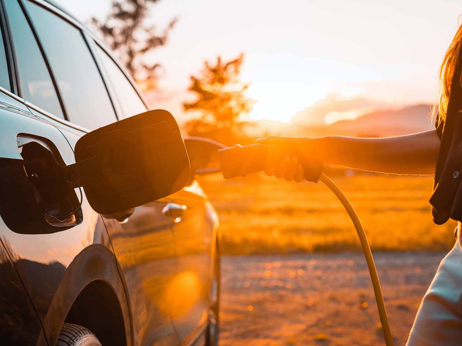 Kvinde sætter ladestik i elbil. Få en mere afslappende tur med ruteplanlægning af din køretur i elbilen.
