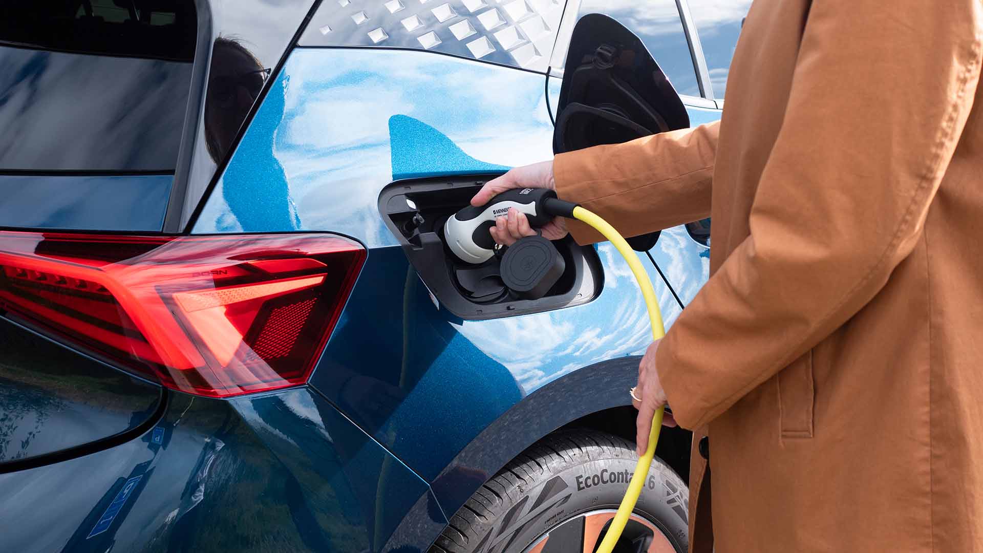 Person sætter ladestik i blå elbil. Må man sjatlade en elbil eller skader det batteriet? Få svaret her.