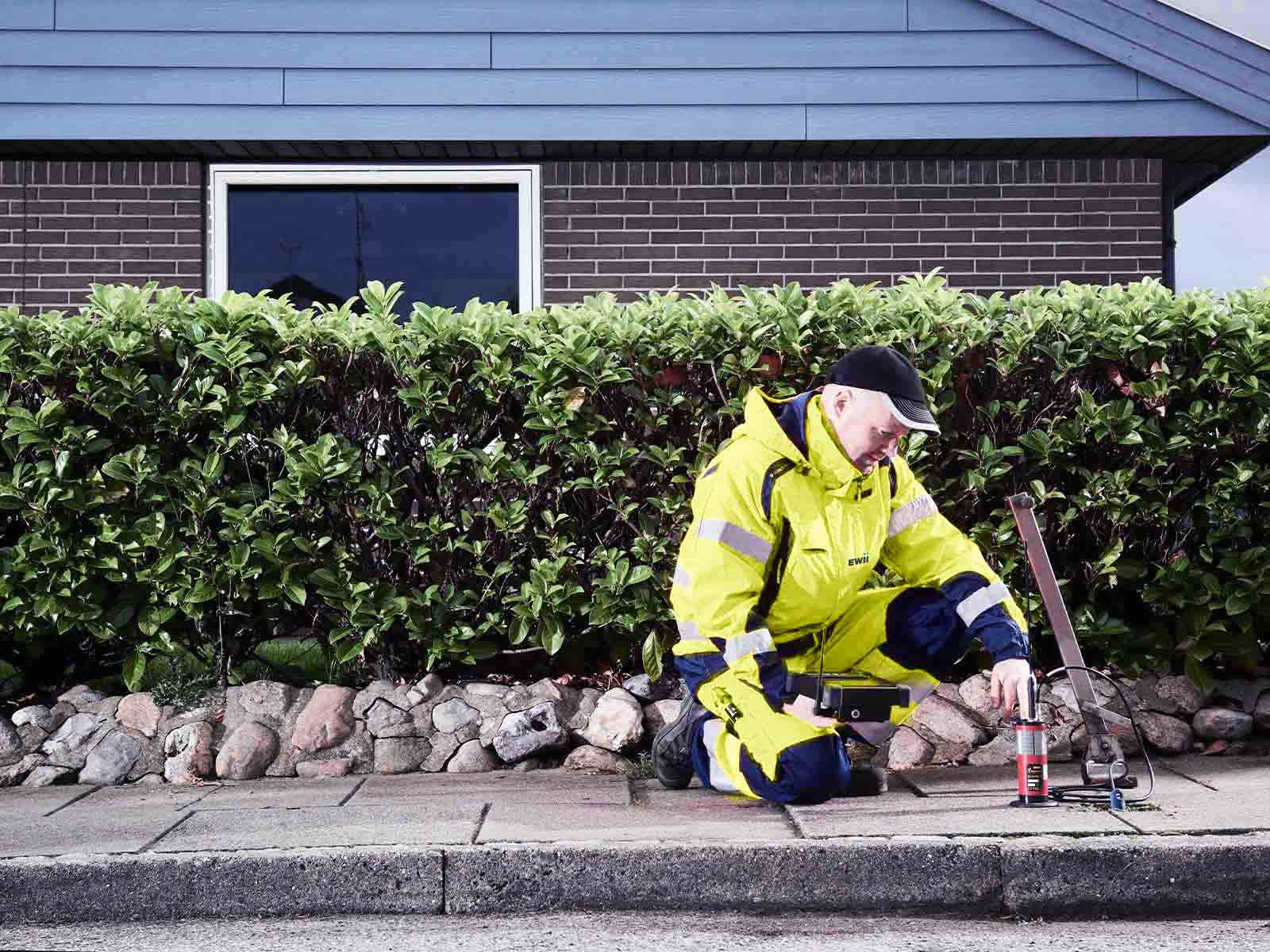 Montør søger efter vandlækager i fortov foran parcelhus