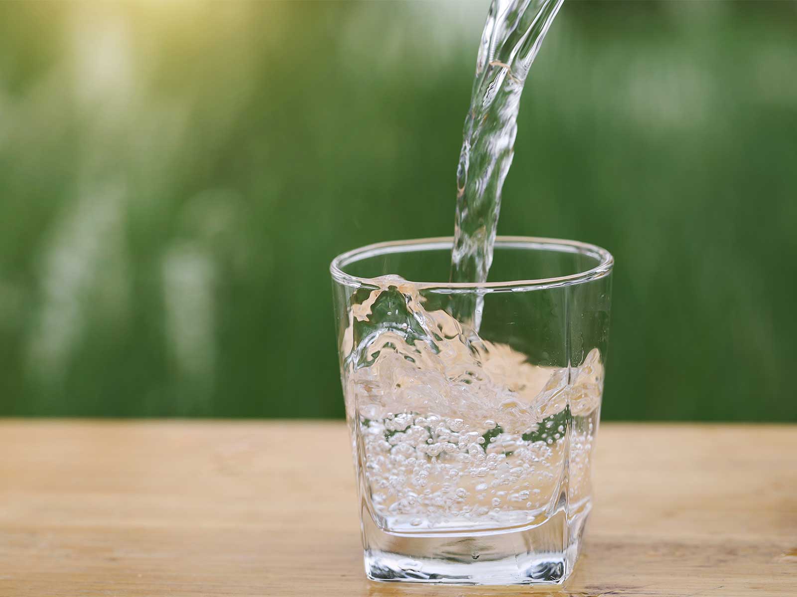 Drikkevand hældes i glas som står på et bord med en grøn baggrund.