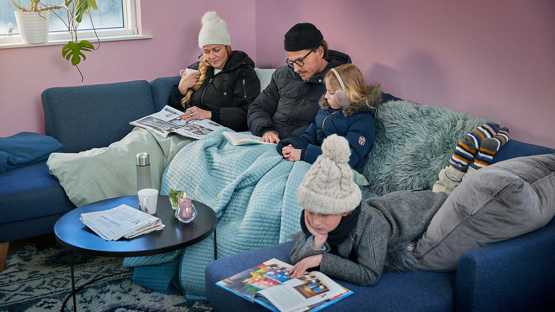 Frysende familie sidder i sofa med tæpper og vintertøj