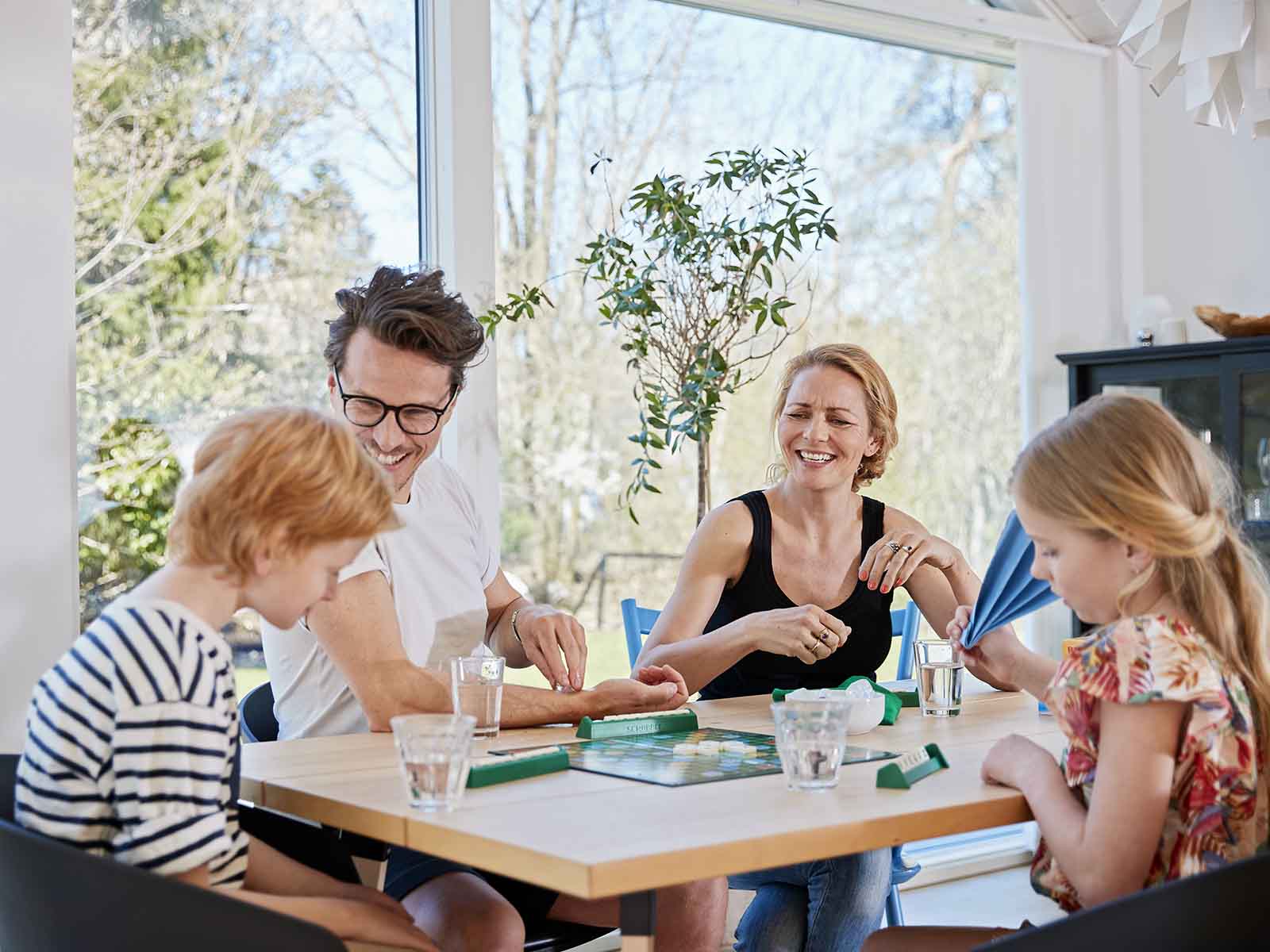 Familie sidder ved spisebord og hygger med at spille brætspil.