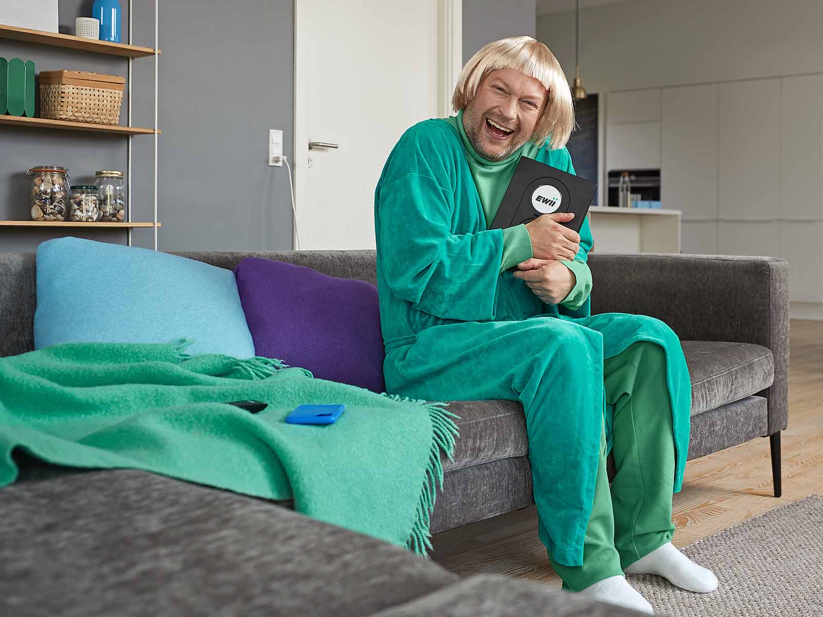 Mand i morgenkåbe og paryk sidder på sofa og krammer en ladeboks fra EWII