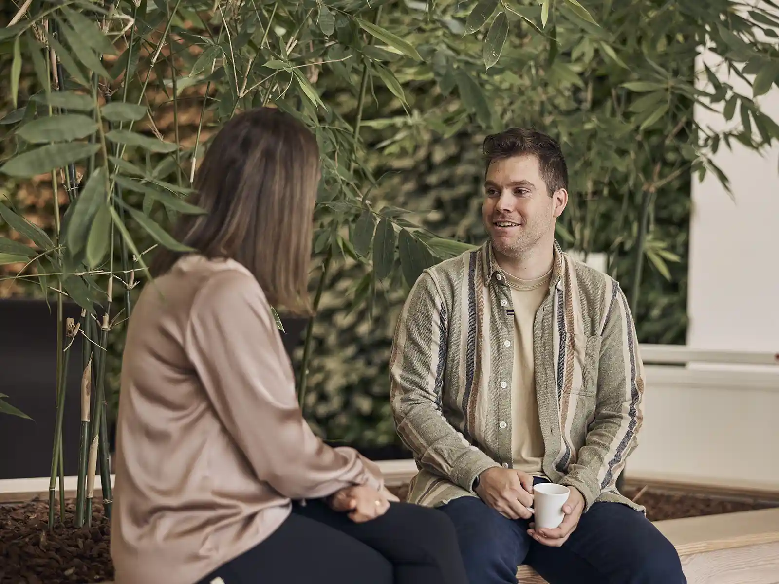 Kvindelig og mandlig EWII kolleger holder møde ved planter og drikker kaffe