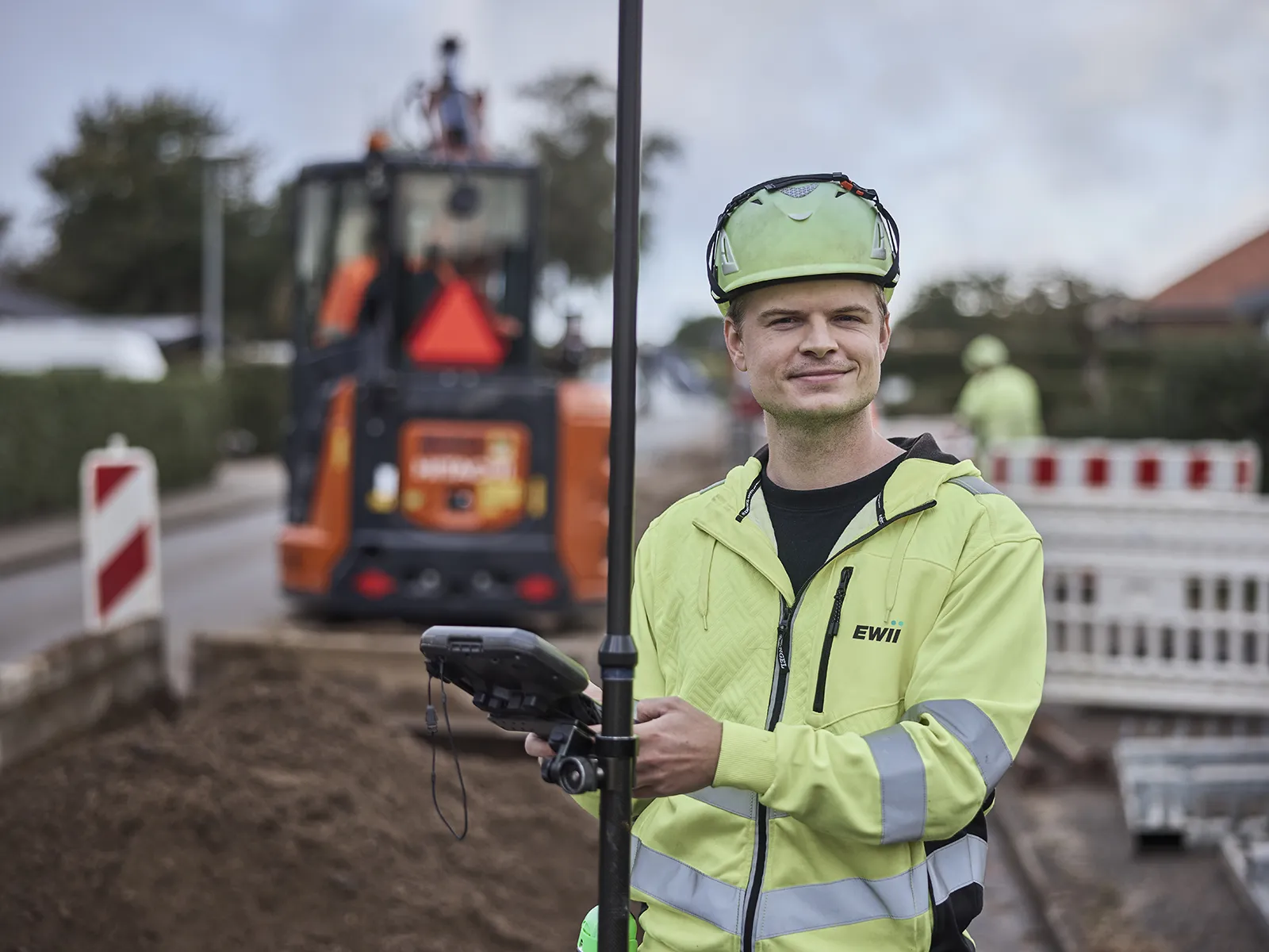 Tekniker med måleapparat kigger i kamera og smiler.