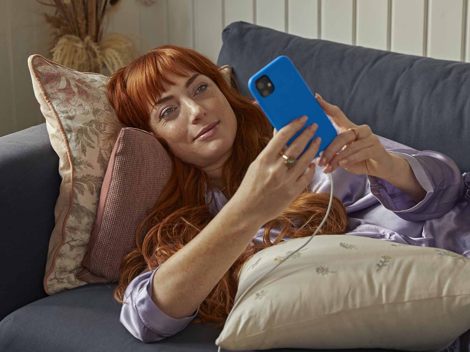 Kvinde ligger i sofa og kigger på sin mobil. Hun er ved at skifte internetudbyder til EWII. Få guiden til, hvordan du skifter internetudbyder uden besvær her.