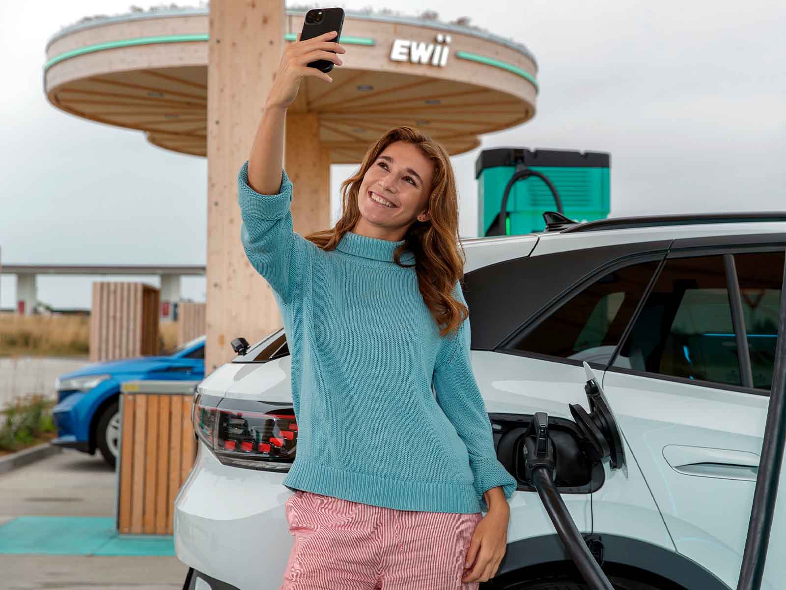 Kvinde tager selfie ved elbil på lynladestation
