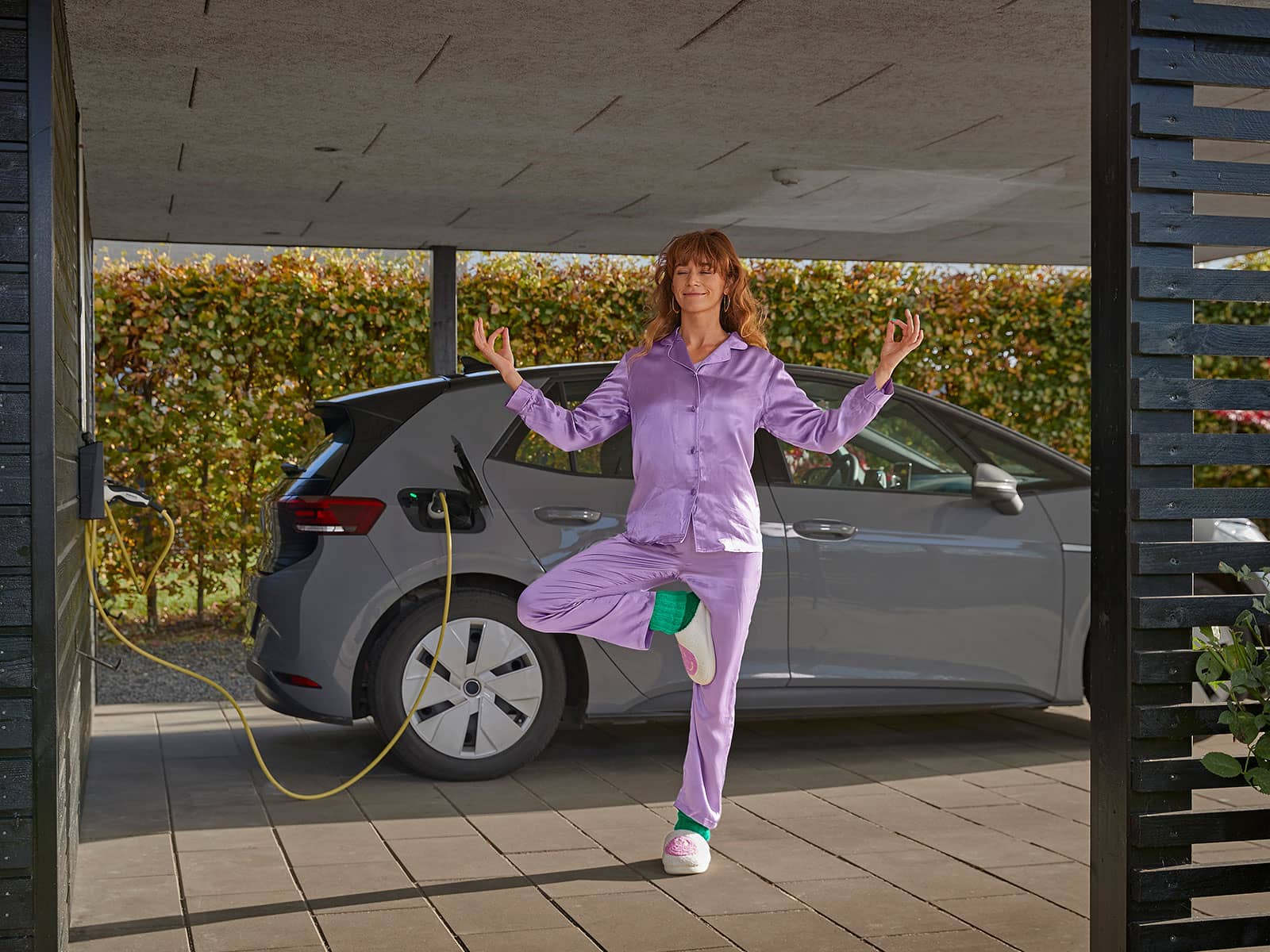 Dame i lilla pyjasmas laver yoga i sin carport mens hendes elbillader med Lade El fra EWII