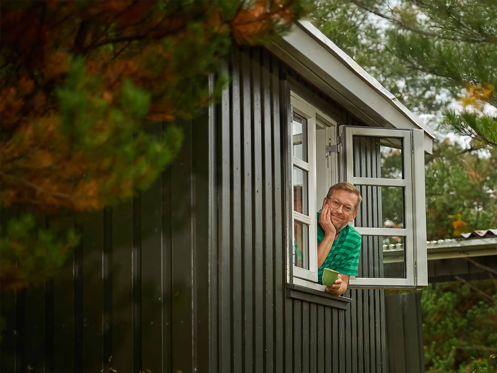 Mand læner sig ud af vindue med kaffekop i hånden og glæder sig over, at han har en Grøn Timepris elaftale