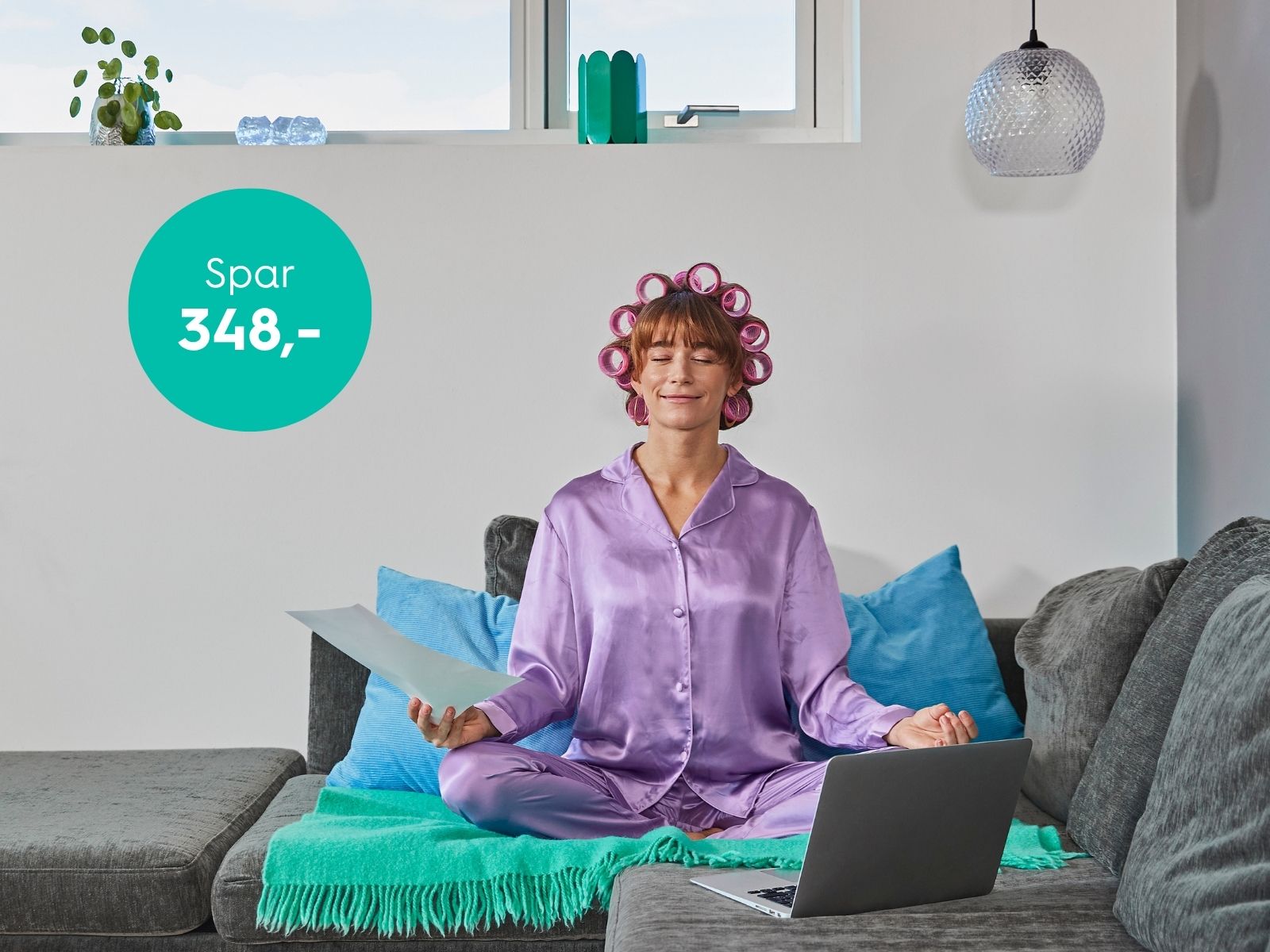 Kvinde i lilla pyjamas sidder i skædderstilling i sin sofa med bærbar og og elregning. Hun er helt afslappet, da hun har Plus El til 0 kr. i abonnement i 12 måneder hos EWII.