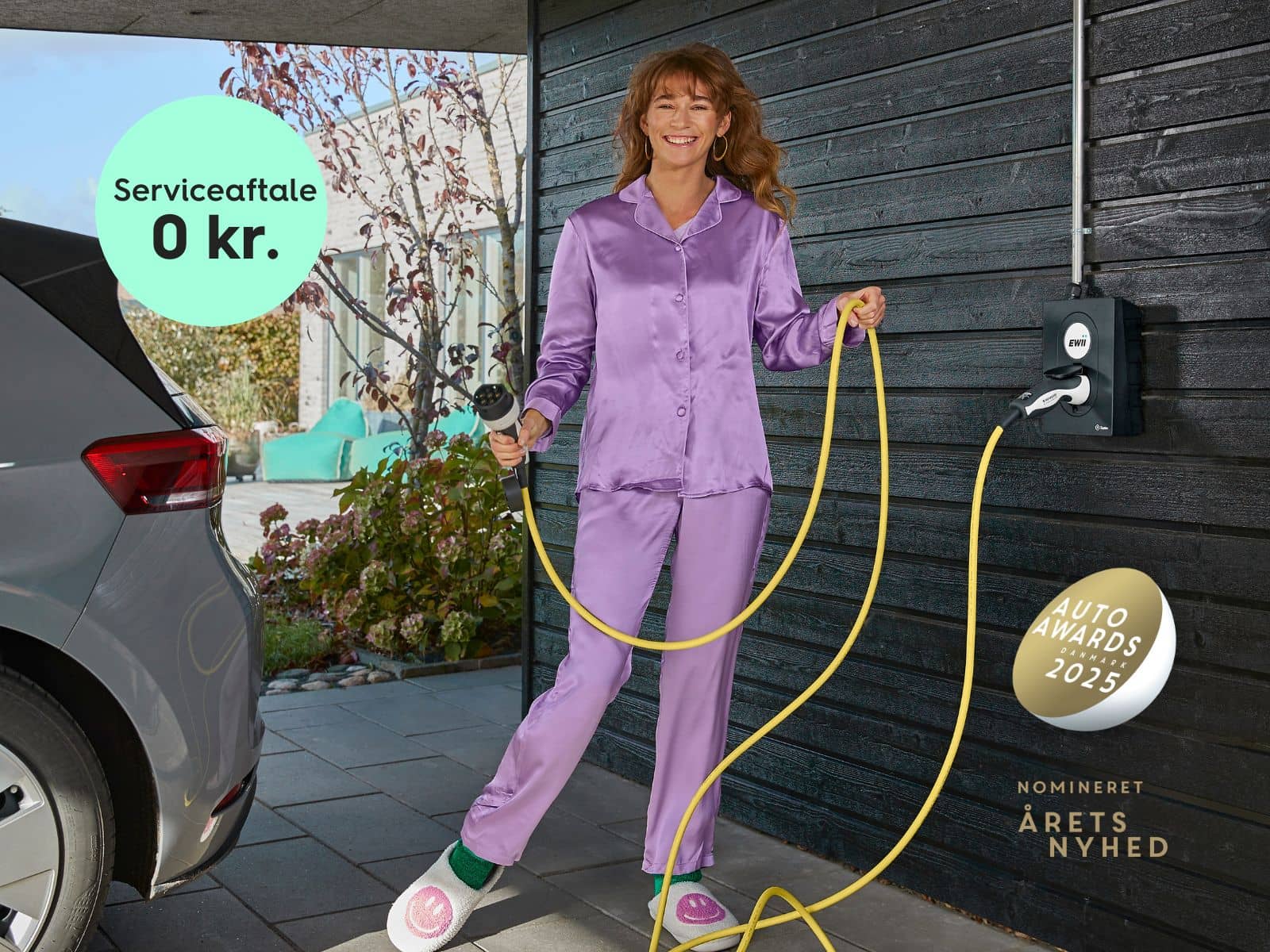 En kvinde i lilla pyjamas skal til at lade sin elbil i en ladeboks fra EWII, som er nomineret til årets nyhed 2025 hos Auto Awards Danmark.