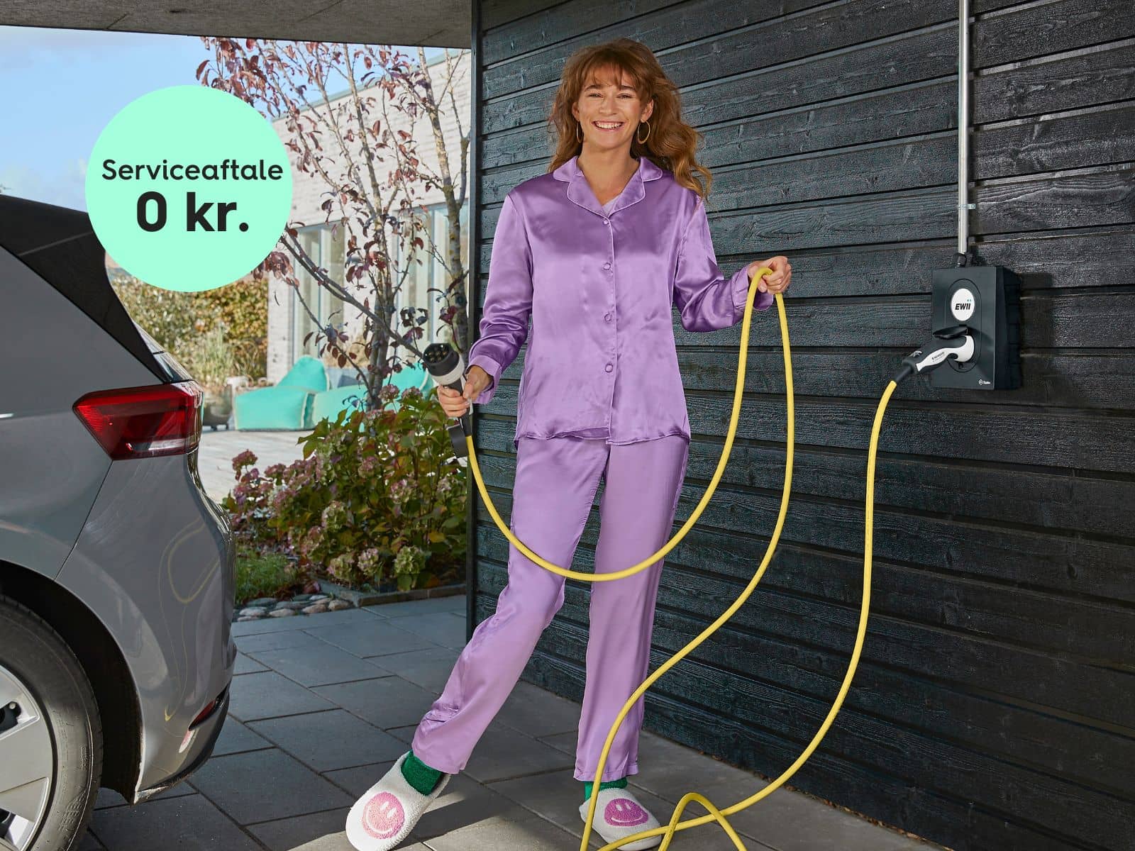 Kvinde i lilla pyjamas gør i sin carport og er glad, da hun har en serviceaftale til 0 kr. pr. måned fra EWII