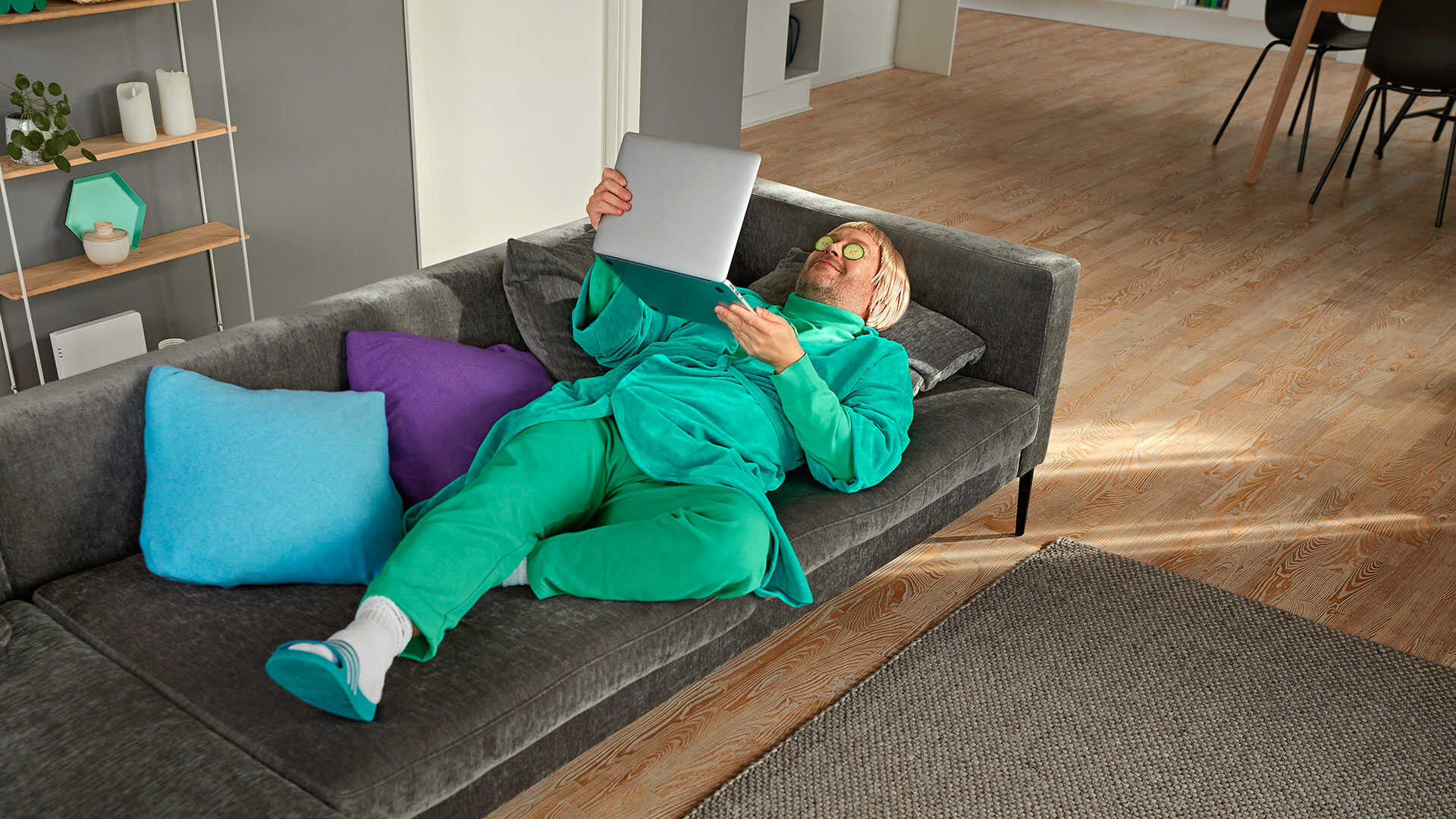 Mand ligger på sofa med agurker på øjnene og en bærbar pc