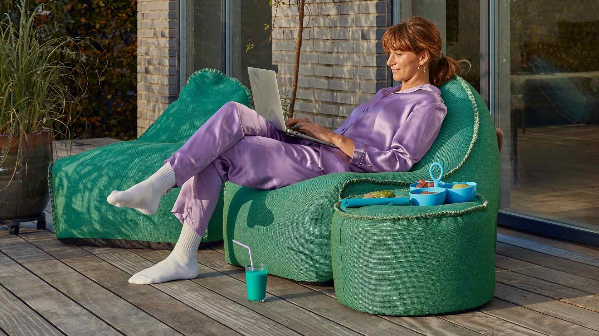 Kvinde sidder i sækkestol på træterrasse med PC i skødet. Hun har bestilt internet fra EWII, så hun bare kan læne sig tilbage og slappe af. Få stabilt bredbånd til hele familien nu.