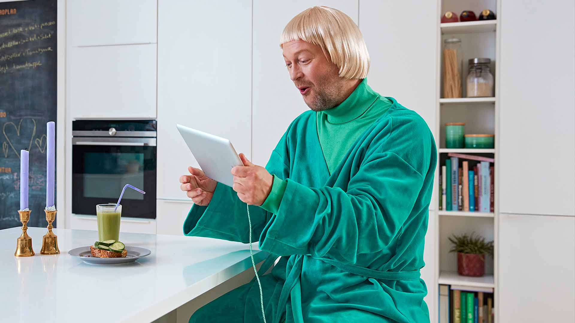 Glad mand i morgenkåbe sidder med tablet ved køkkenø. Han bestiller internet fra EWII og få et gavekort på 400 kr. til oplevelser og shopping.