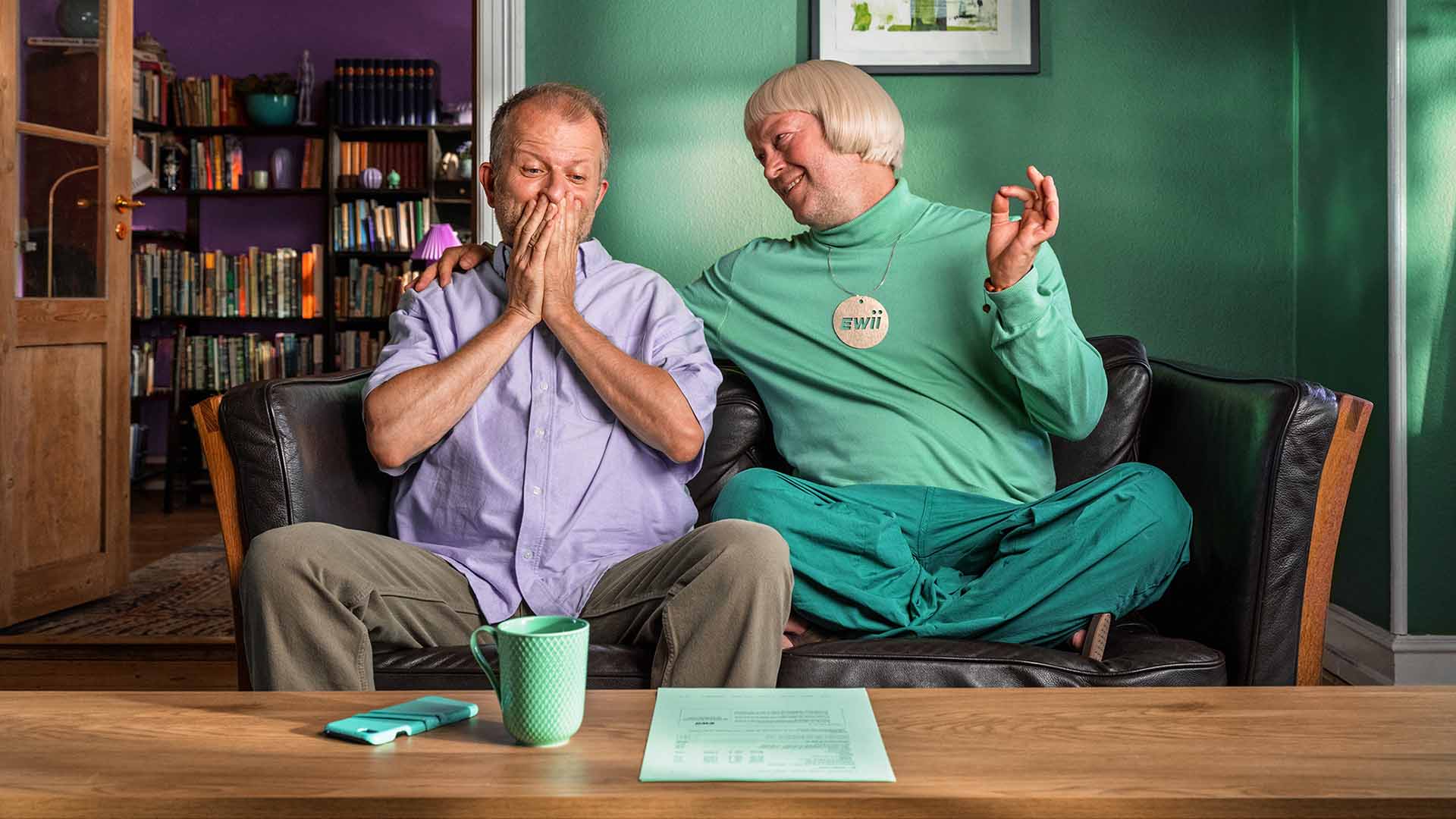 Mand sidder i sofa med EWII-manden. Han er glad fordi han har fået en enkel elregning