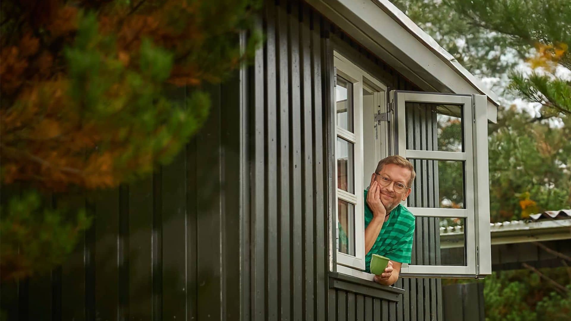 Mand hænger ud af vindue med kaffekop i hånden og glæder sig over at spare 1.000 kr. på Grøn Timepris.
