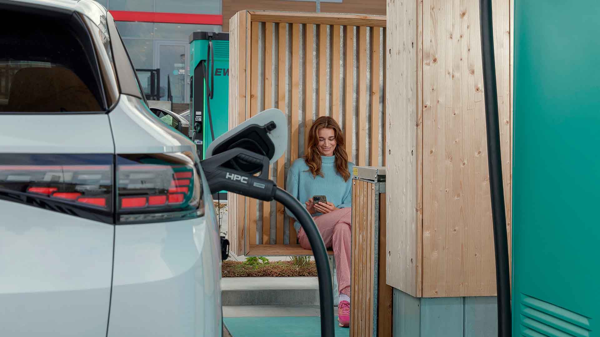 Kvinde sidder med mobil ved elbil der lynlader. Hun undersøger hvor lang tid tager det at lade en elbil op. Vi giver dig svaret her.