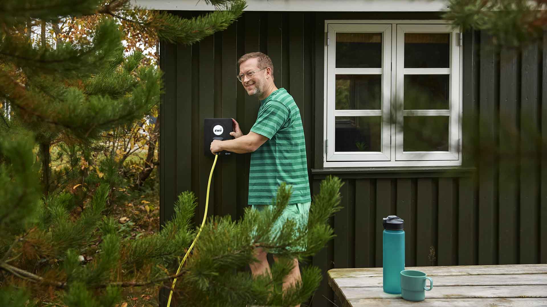 Mand sætter ladestik i ladeboks ved sommerhus. Med en ladestander til sommerhuset fra EWII bliver dit sommerhus mere attraktivt for udlejning og mere værdi, hvis du ønsker at sælge en dag.