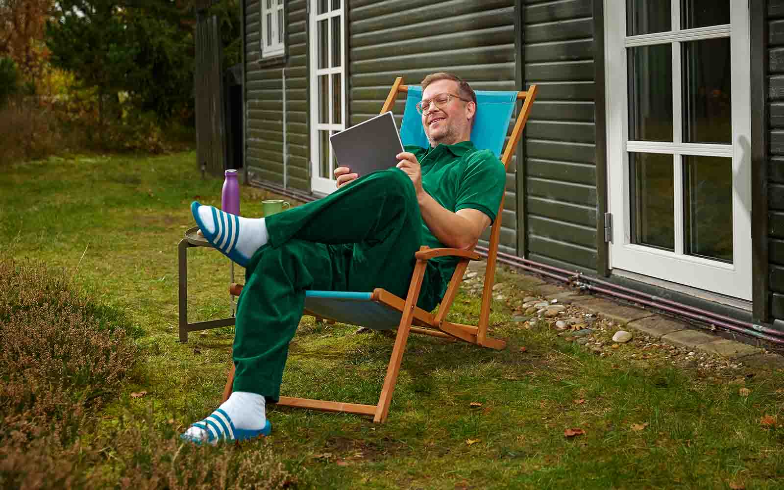 Mand ligger i havestol ved sit sommerhus og kigger på sin tablet.
