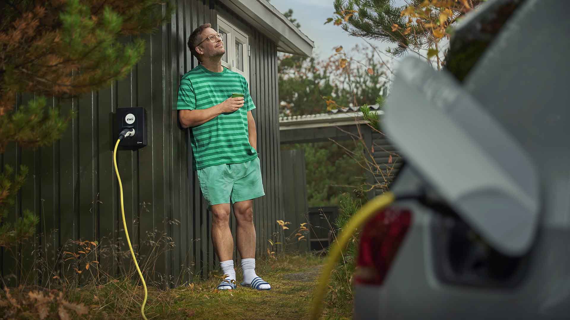 Mand læner sig op ad sit sommerhus imens elbilen bliver ladet op af en EWII ladeboks