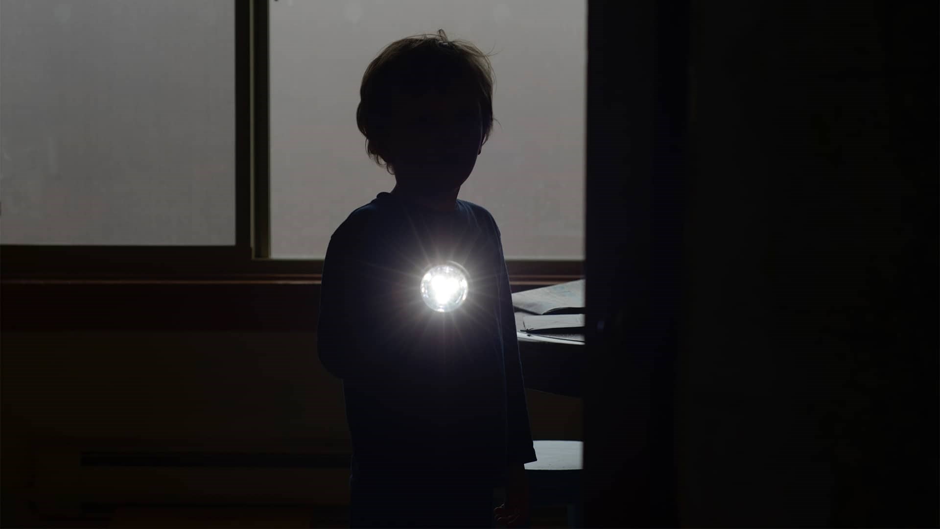 Dreng i mørke lyser med lommelygte grundet strømsvigt