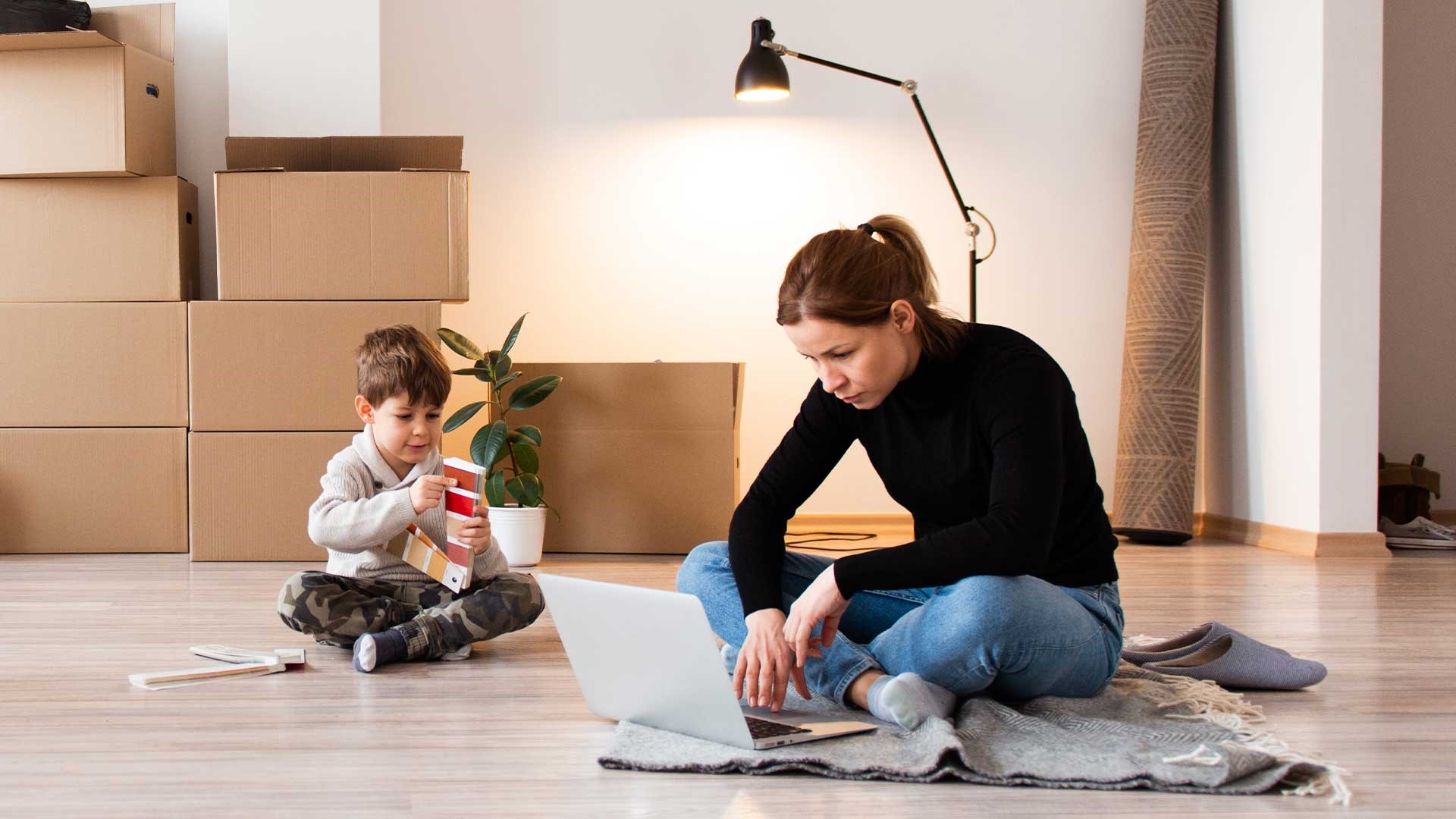 Mor og søn sidder på gulvet med computer og flyttekasser