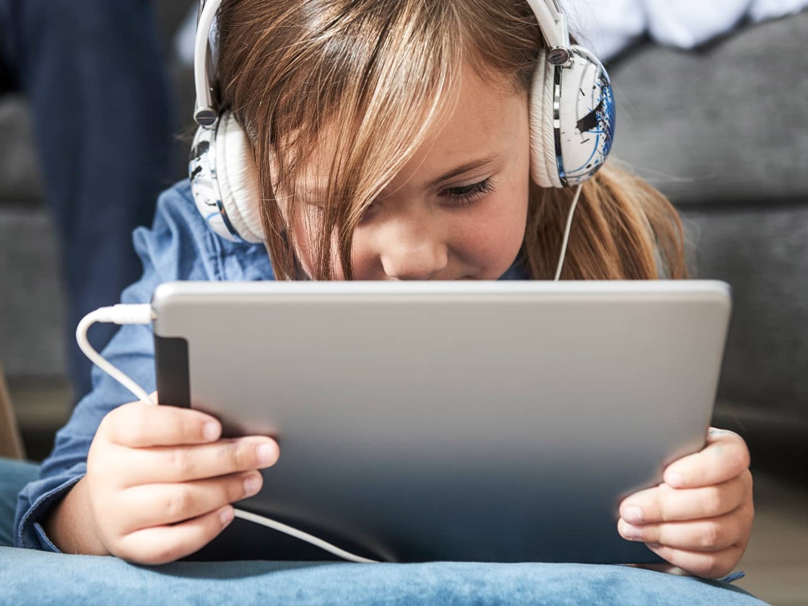 Pige ligger på gulvet med ipad og høretelefoner på og surfer sikkert på nettet, fordi hendes forældre har en digital sikkerhedspakke
