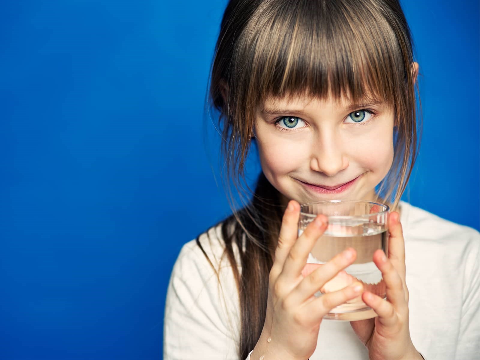 Pige der står med et glas vand i hænderne og smiler uden bekymring for, om der er nok rent drikkevand i fremtiden. Læs om rent drikkevand i Danmark og rent drikkevand i verden.