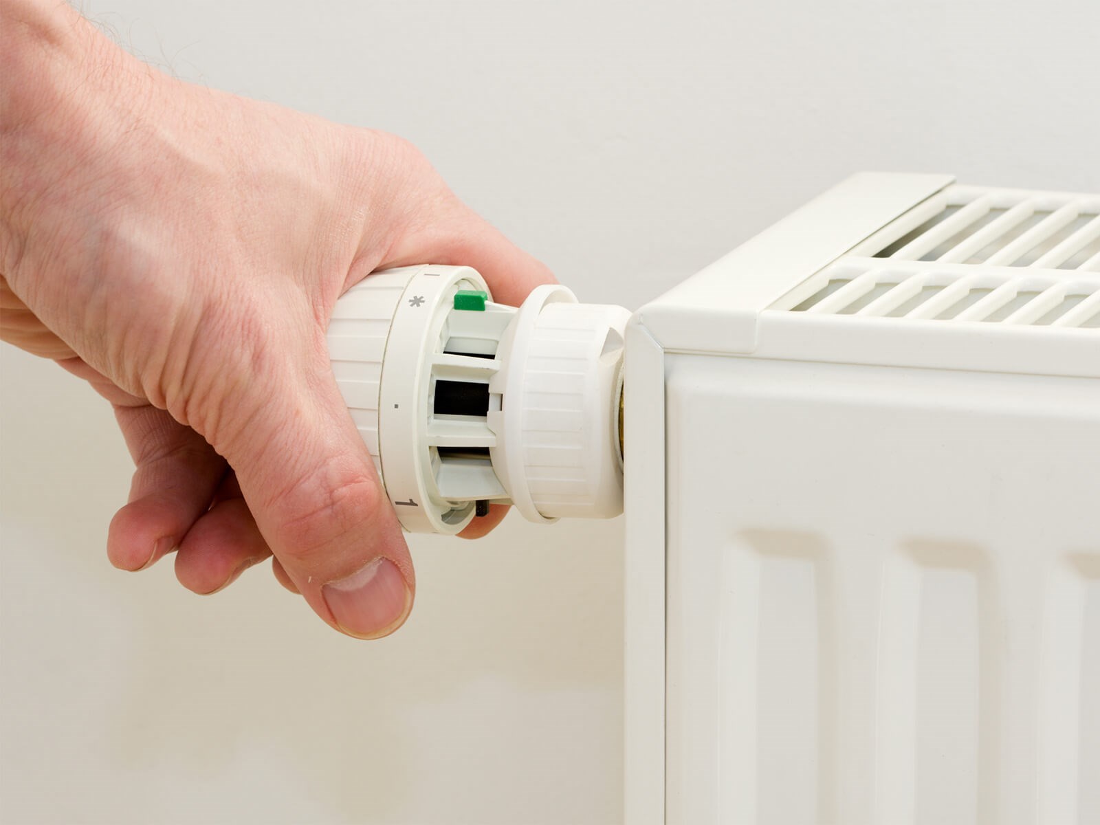 Hånd drejer på radiator. Skru ned for radiator ved udluftning i hjemmet. Hvor længe skal man lufte ud? Gør det af 5-10 minutters varighed.